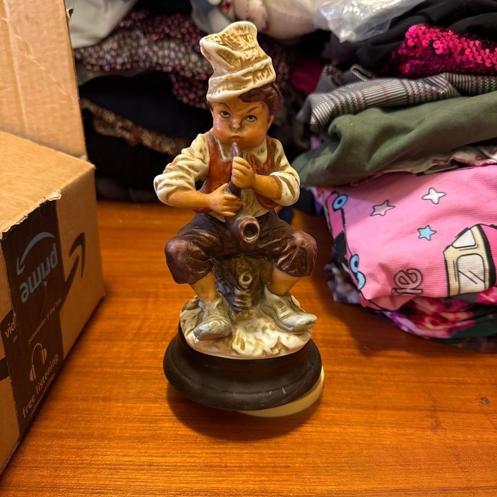 vintage music box figurine depicts a young boy sitting on a stump playing a horn